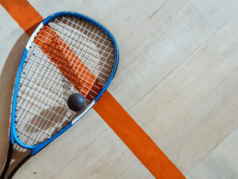 Ein Squash-Schläger und ein Squash-Ball liegen auf dem Hallenboden.
