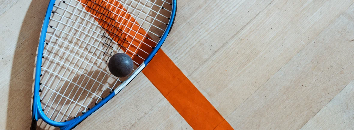 Ein Squash-Schläger und ein Squash-Ball liegen auf dem Hallenboden.
